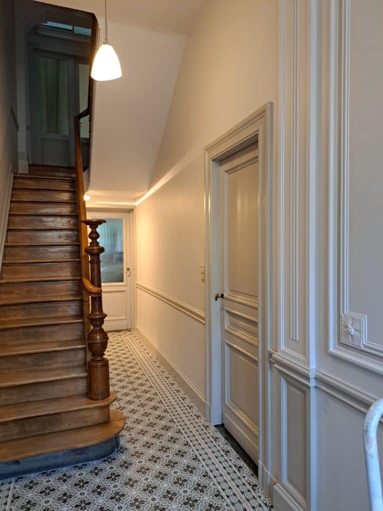 Hall avec escalier en bois et murs clairs à moulures.